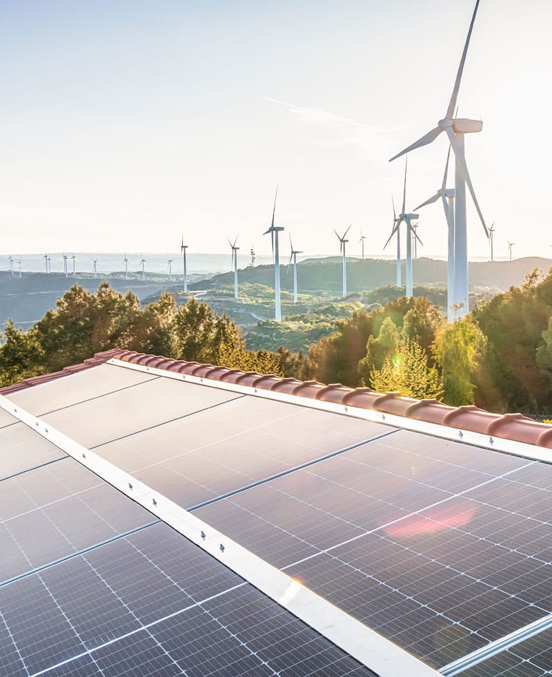 Rooftop solar panels with wind turbines on hillside, representing distributed energy resource (DER) integration.